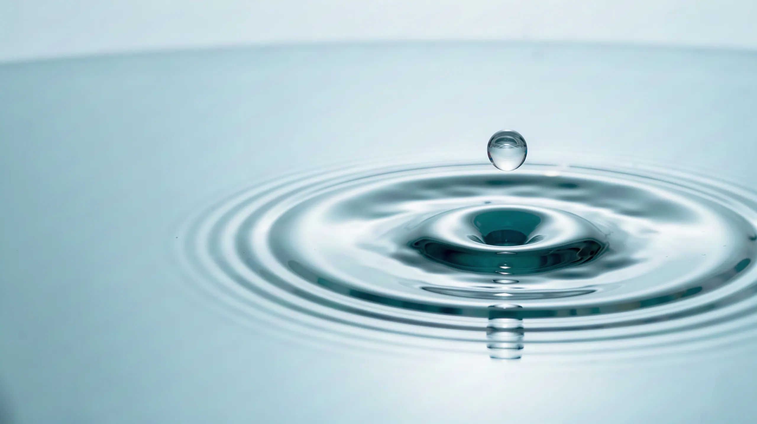 A water drop falling into calm water, forming concentric rings